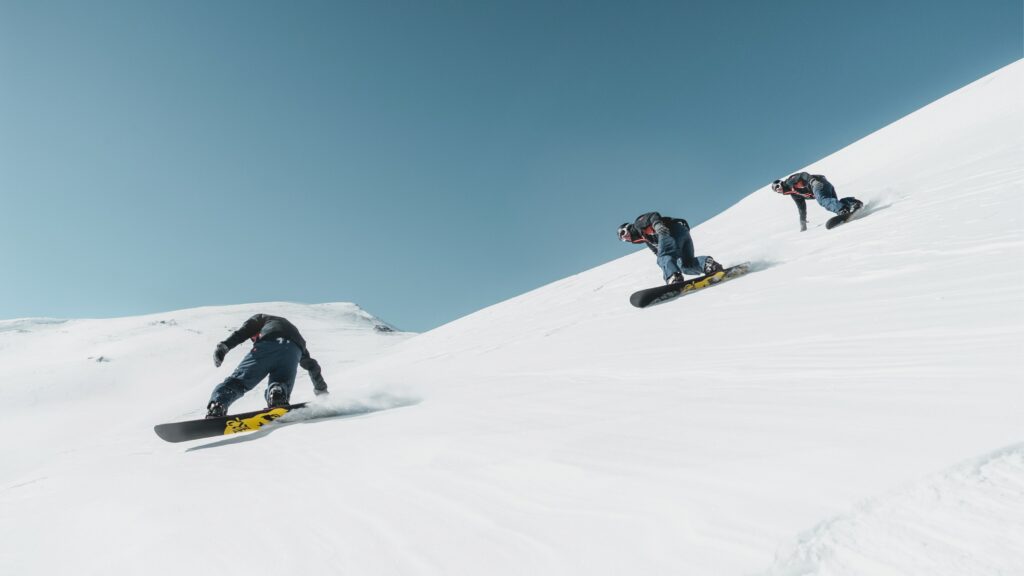 Three people snowboarding down a mountain under a blue sky