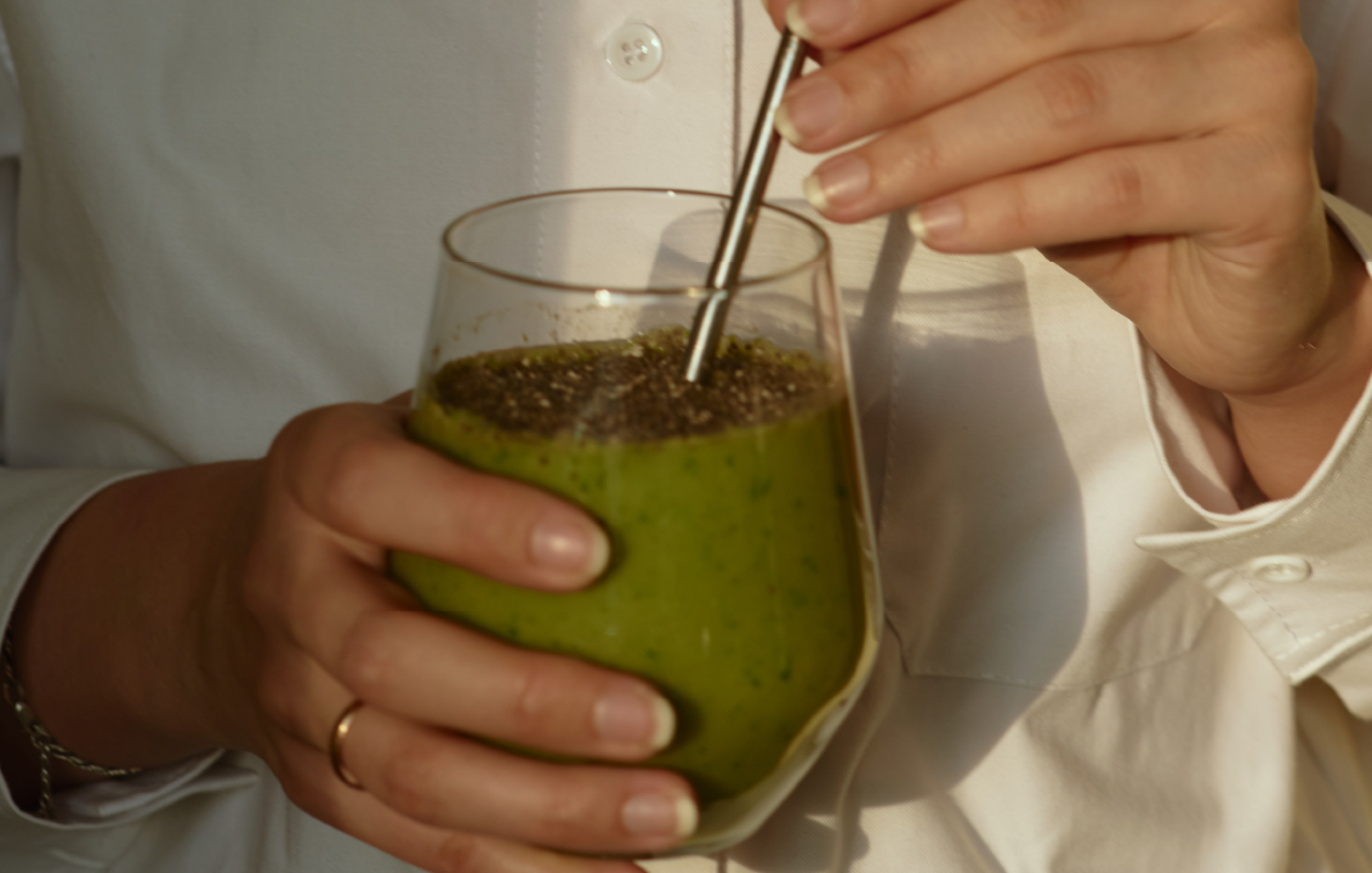 green smoothie in a glass with a metal straw held by a 30-something